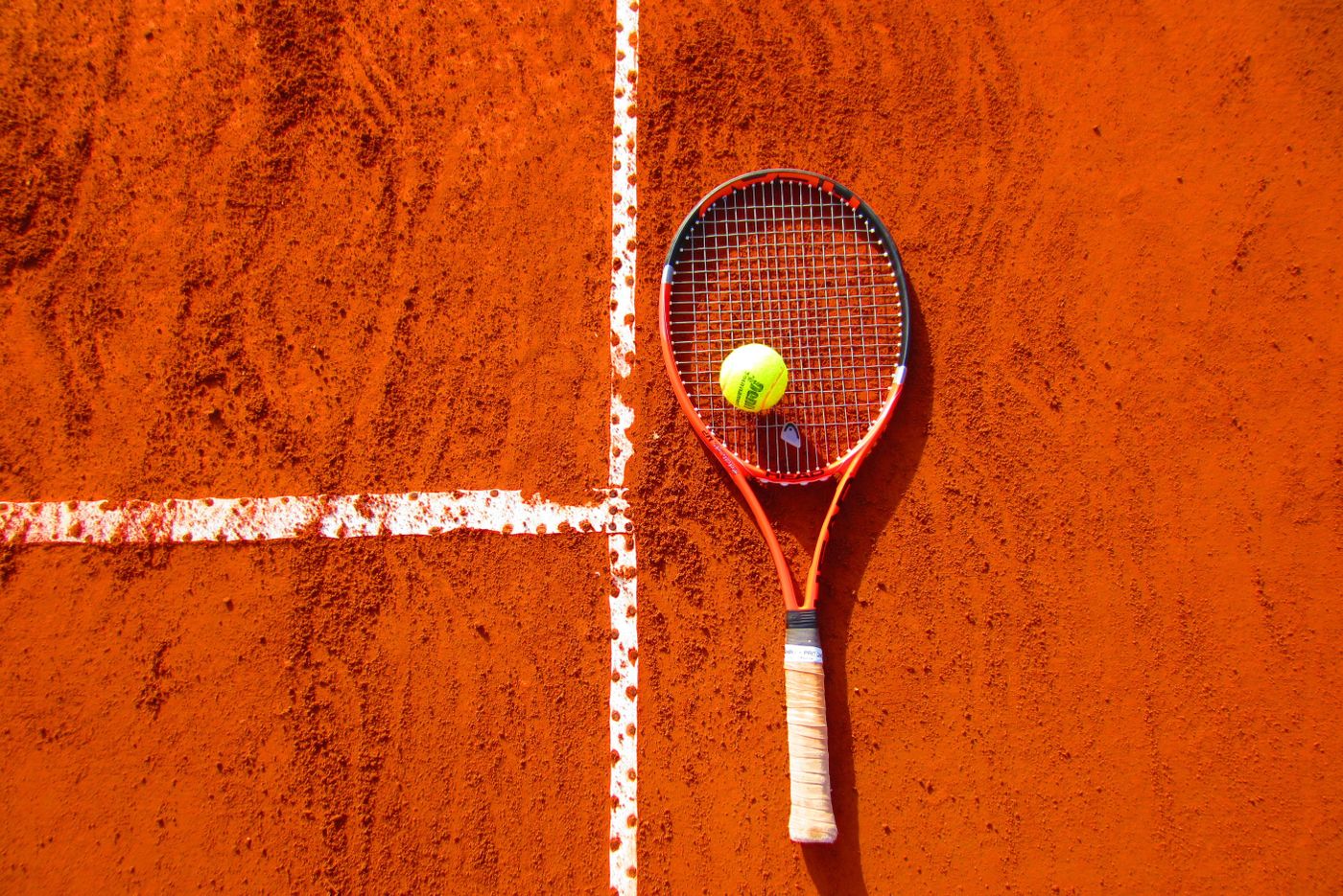 Tennis racket and ball on a clay court — stringbed close-up theme